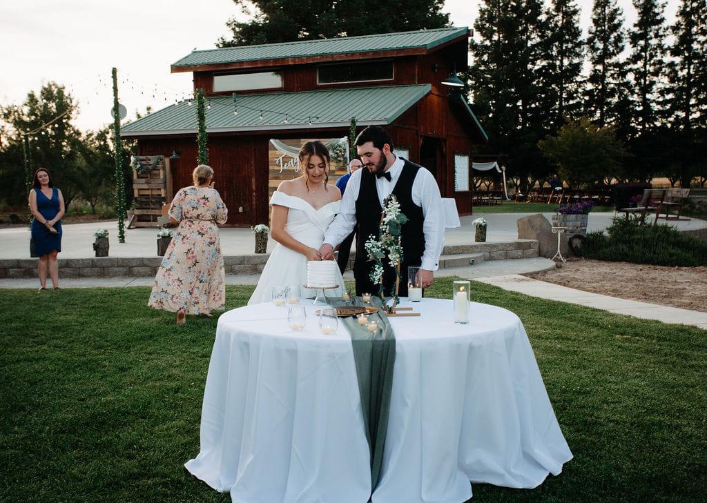 A couple cutting their cake on the lawn in front of the barn