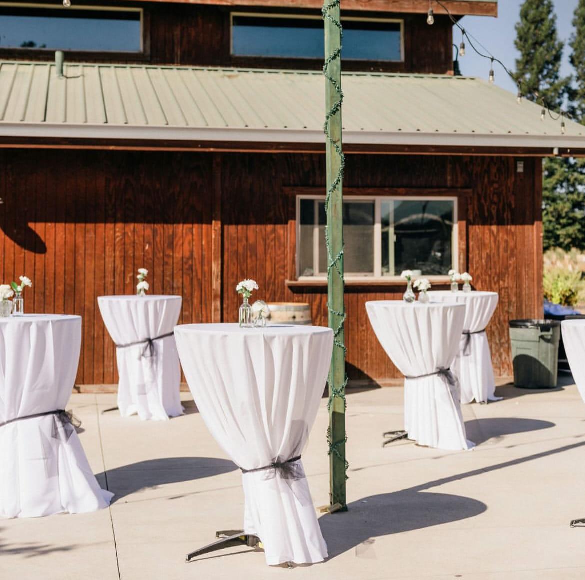 Cocktail tables in white linen set out along the barn