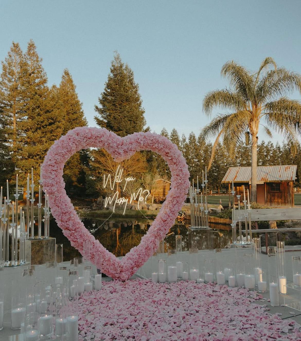 A pink floral heart arch and candlelight at the water's edge