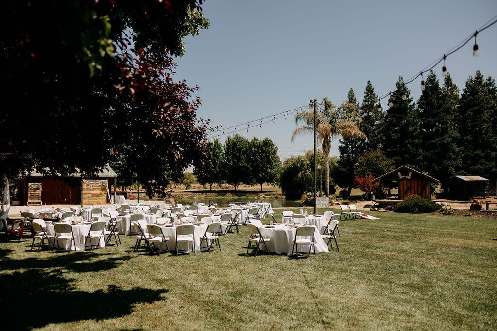 Round tables set on the lawn beneath string lights on a clear afternoon