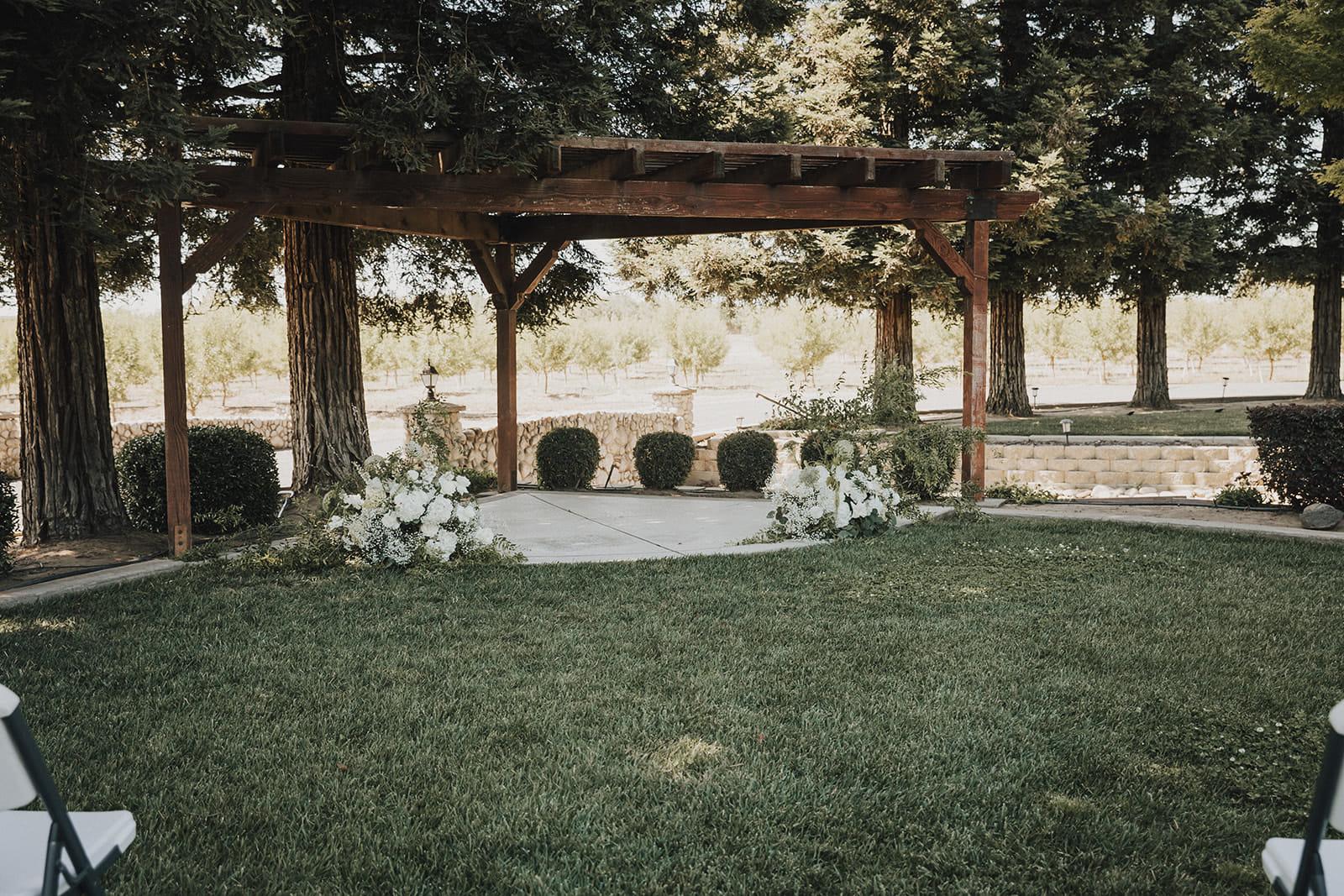 The ceremony pergola dressed with white florals, chairs waiting on the lawn
