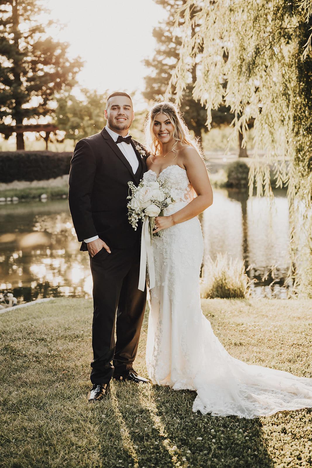 The newlyweds on the lawn beside the pond, late afternoon light behind them