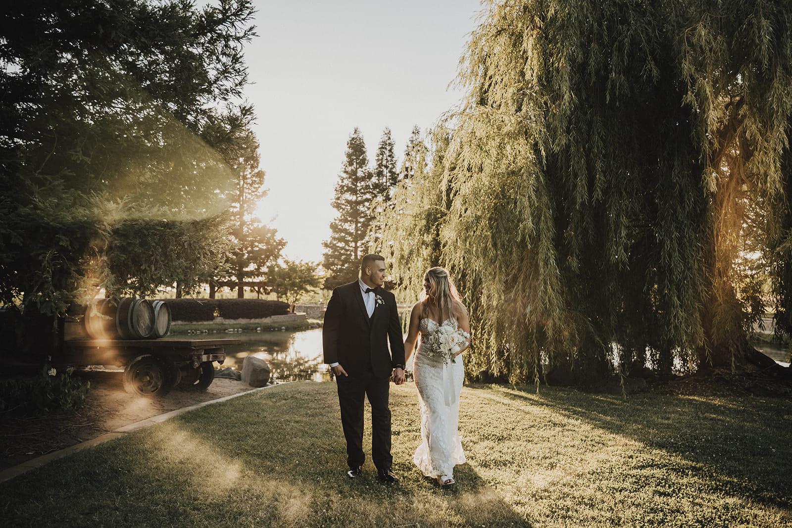 The couple walking hand in hand past the willow and the pond