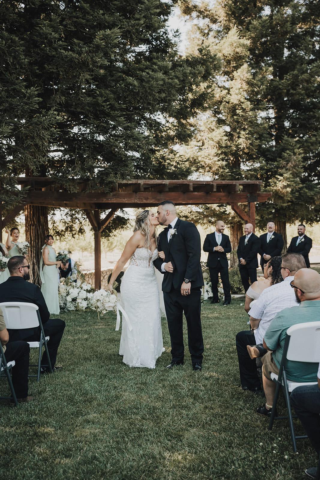 Their first kiss under the pergola as guests look on