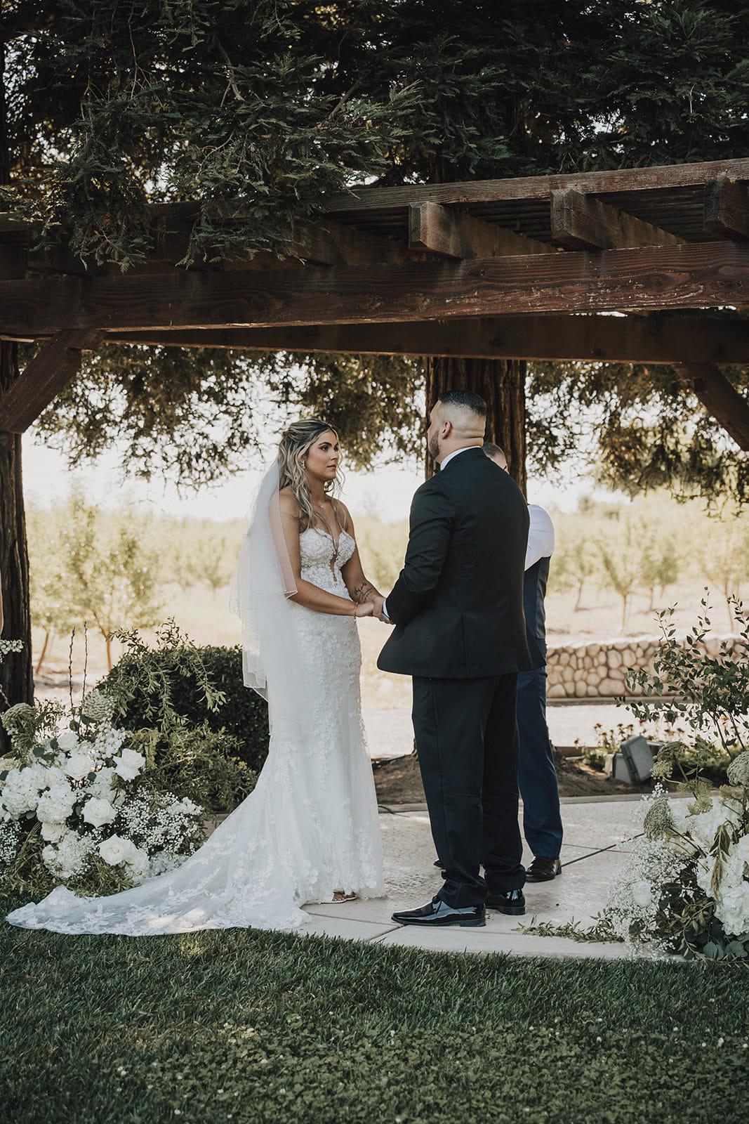 The couple holding hands beneath the pergola during their vows