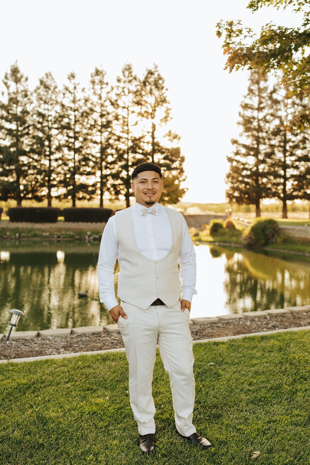 The groom in an ivory tux at the edge of the pond
