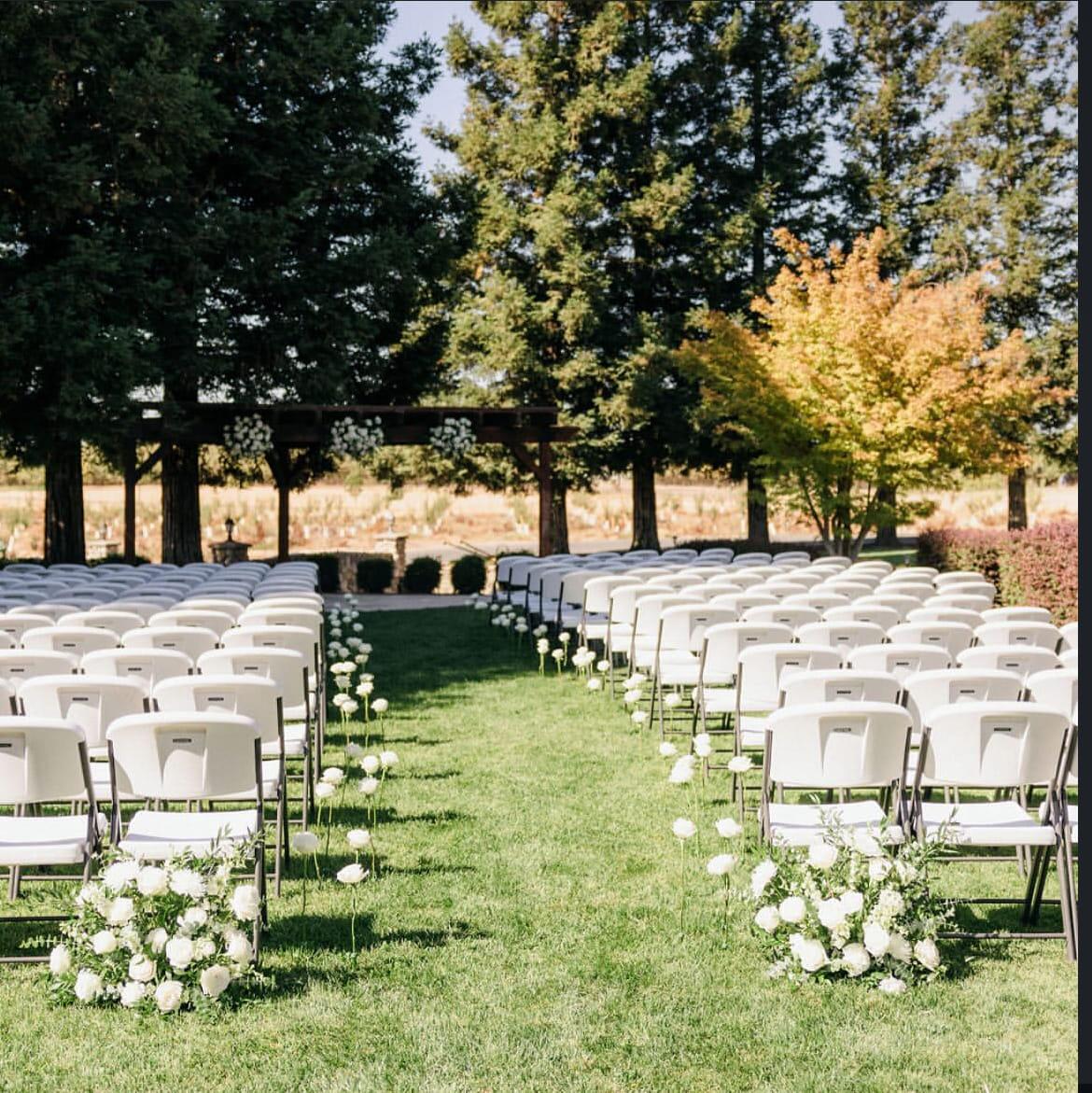 White garden chairs lining a grass aisle edged with white roses