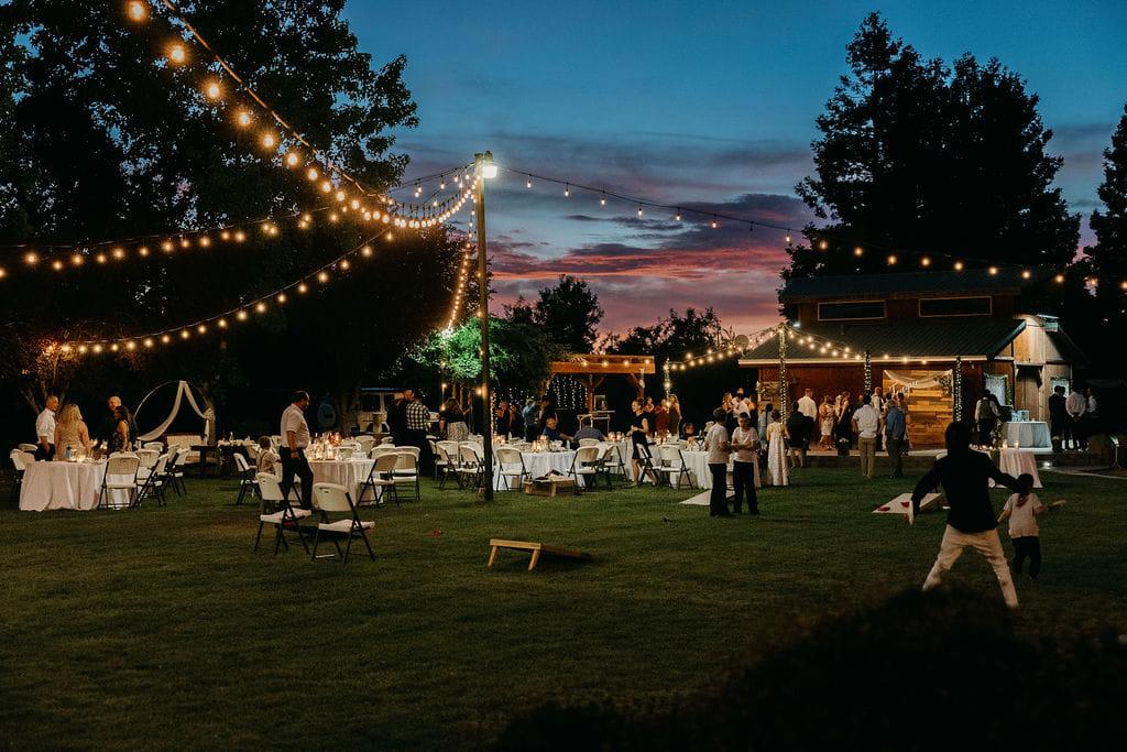 Guests at round tables under string lights as the sky turns pink